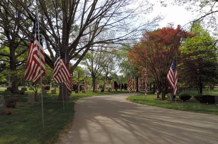 A row of  flags line either side of the road inside Pawtuxet Memorial Park . 