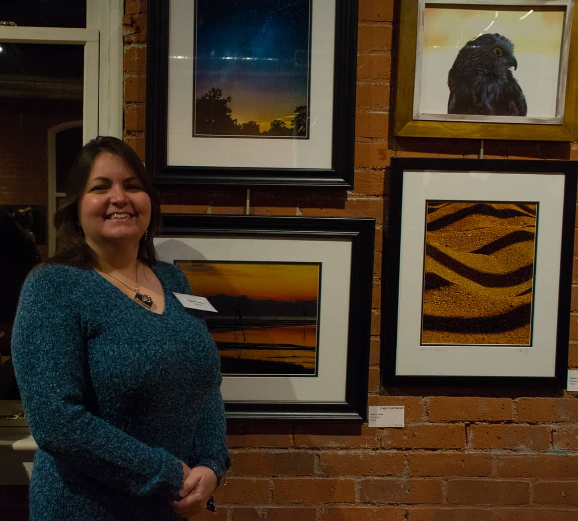 Mary Carlos with her photographs, "Cape Cod Sunset" bottom and "Milky Way and Meteors" at WMOA Wednesday night.
