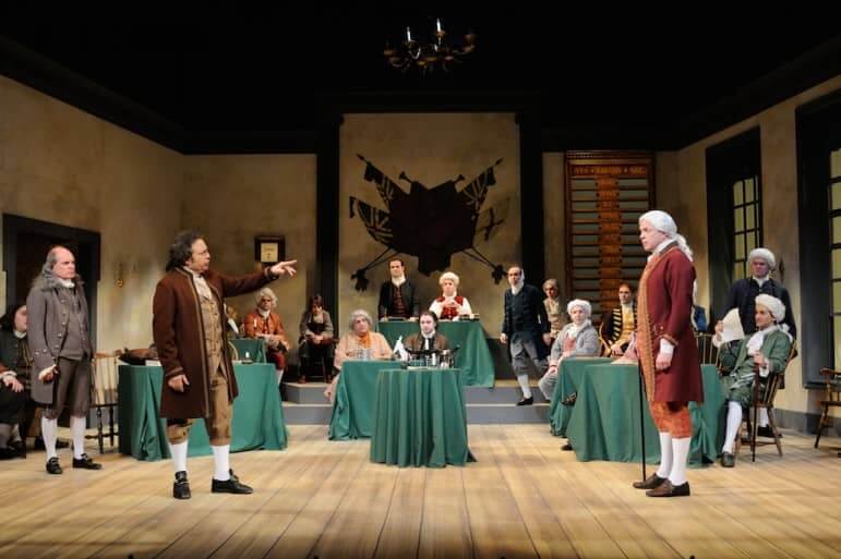 [CREDIT: Mark Turek] Lou Ursone (left) as John Adams confronts Christopher Swan (right) as John Dickinson, while Ben Franklin played by Mark S. Cartier (far left) and other members of congress look on during 1776.