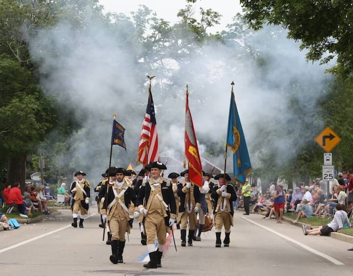 [CREDIT: Beth Hurd] Members of the Lexington Minutemen emerge from the smoke of their recently fired muskets, walking along the red, white and blue-striped parade route on Saturday, June 11.