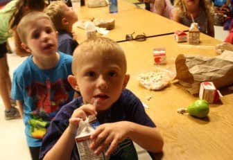 [CREDIT: Beth Hurd] Pierce Leonard, age 6, enjoys his TruMoo chocolate milk after eating some of his chicken salad lunch on Tuesday, July 28. Behind him is Kellen Barnes, 6, who brought a Lunchables from home. 