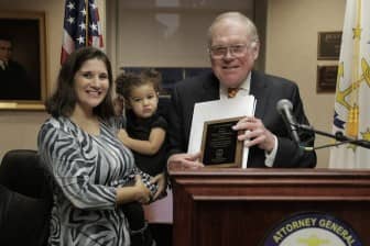 [CREDIT: RIAG} Former Attorney General Dennis Roberts presents the Justice Award for Crime Prevention, given in his name) to Warwick resident and RI State Trooper Anthony Washington. Accepting on his behalf was Trooper Washington’s wife Rebecca and daughter Ava.