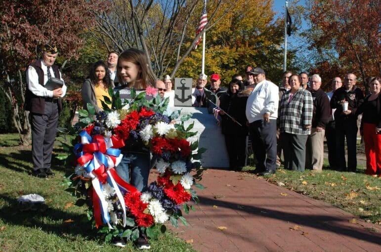 [CREDIT: Rob Borkowski] Hailey Norman, 6, holds a wreath for the memorial at Veterans Memorial Park near Veterans Memorial Middle School Friday.