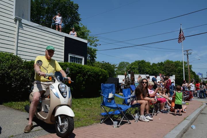 [CREDIT: Rob Borkowski] At left, Tom Walsh parks his scooter as Erin Walsh and Alison O'Donnel watch from the roof of Noon Design at the start of the 2017 Gaspee Day Parade.