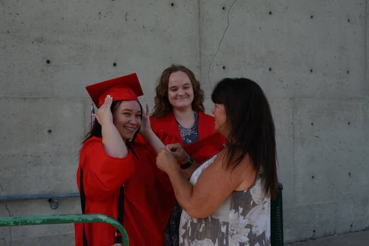 [CREDIT: Rob Borkowski] Kellie Mascia helped her daughter, Nicole, with her cap and gown as grad Brittney Larkin looked on.
