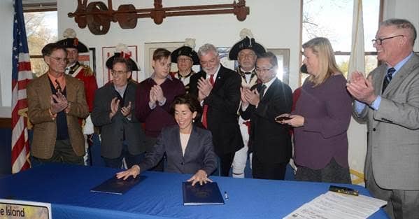 [CREDIT: Daniel Trafford] Gov. Gina Raimondo ceremonially signs legislation creating a special Gaspee Days license plate today during a ceremony at the Aspray Boat House in Warwick. At right are bill sponsors Rep. Joseph M. McNamara (D-Dist. 19, Warwick, Cranston) and Sen. Erin Lynch Prata (D-Dist. 31, Warwick, Cranston), along with Cranston Mayor Allan Fung, third from right, Warwick Mayor Scott Avedisian, fourth from right, Sen. Joshua Miller (D-Dist. 28, Cranston, Providence), second from left, Warwick City Councilman Richard Corley, left, along with members of the Pawtuxet Rangers militia and the Gaspee Days Committee. 
