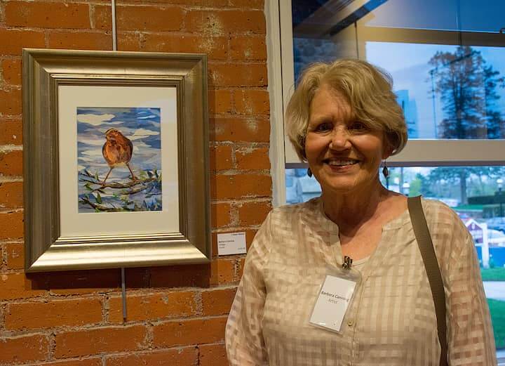 [CREDIT: Mary Carlos] Artist Barbara Canning with her work, "I hear music" during the opening reception for the "Sights and Sounds" juried art exhibit at the Warwick Center for the Arts.