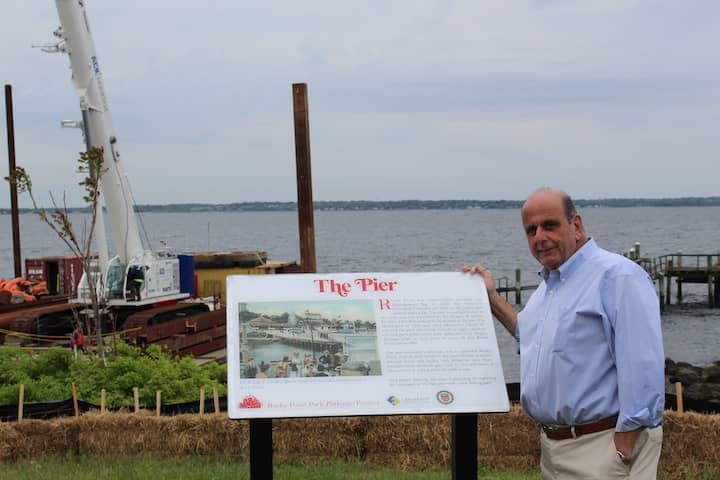 [CREDIT: Mayor Solomon's Offiice] Mayor Joseph Solomon at the start of construction on a new fishing pier at Rocky Point Park. Solomon stands next to a plaque showing the original pier in its heyday.