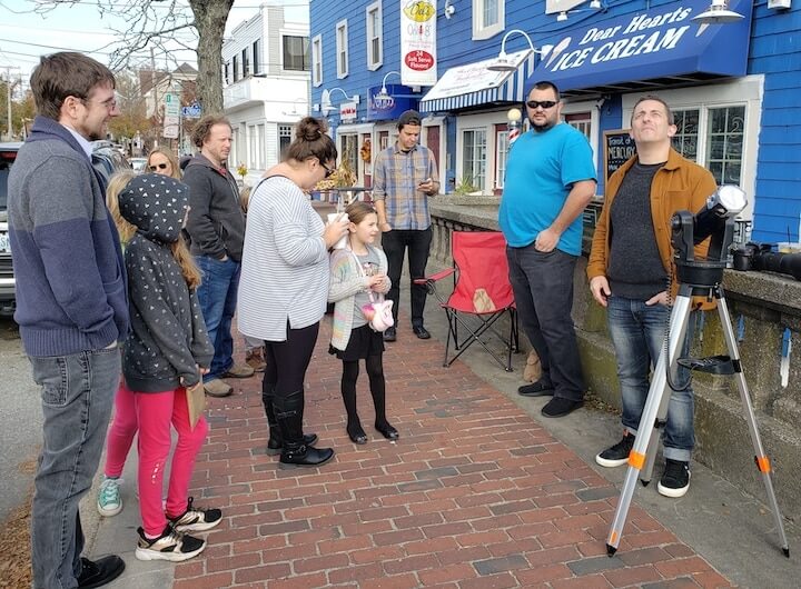 [CREDIT: Mary Carlos] Jason Major, right, glances up at a brief cloud cover to gauge when another view of the Transit of Mercury will be available in Pawtuxet Village Nov. 11, 2019.