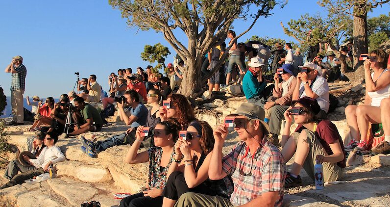 [CREDIT: National Park Service] A crowd uses handheld solar viewers and solar eclipse glasses to safely view a solar eclipse.