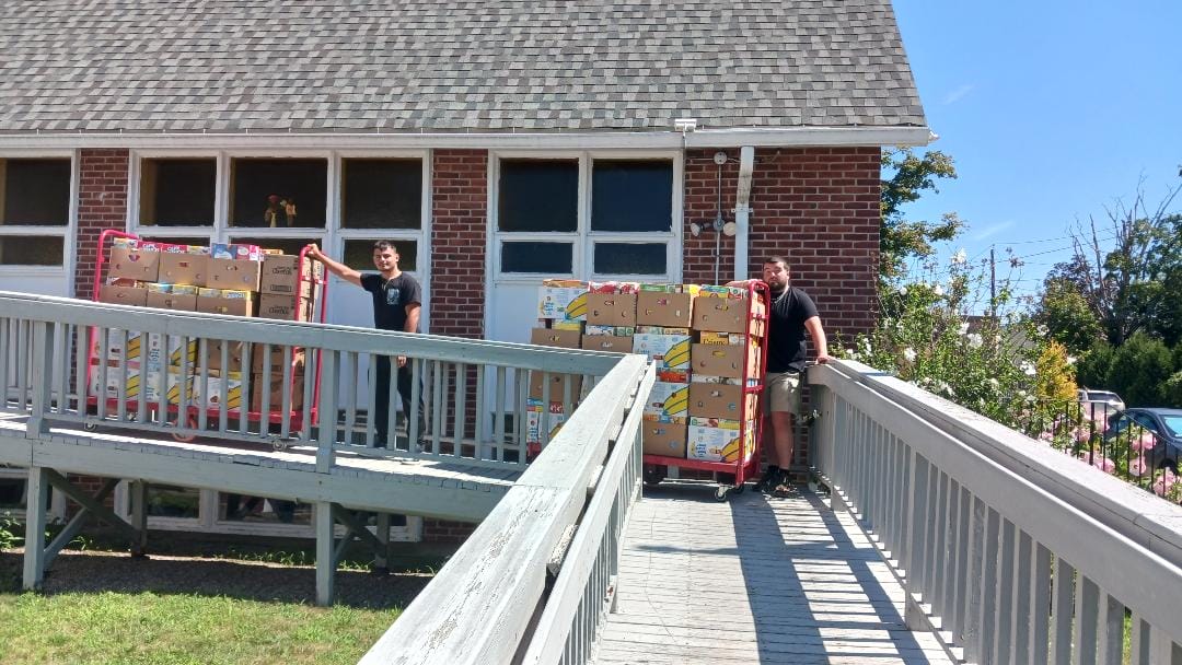 [CREDIT: Lincoln Smith/ Photographic Society of RI] Caden Denton and Jordan Hiatt/Marketplace Supervisor unload cereal from the truck at West Bay Marketplace during the Cereal Challenge food drive.